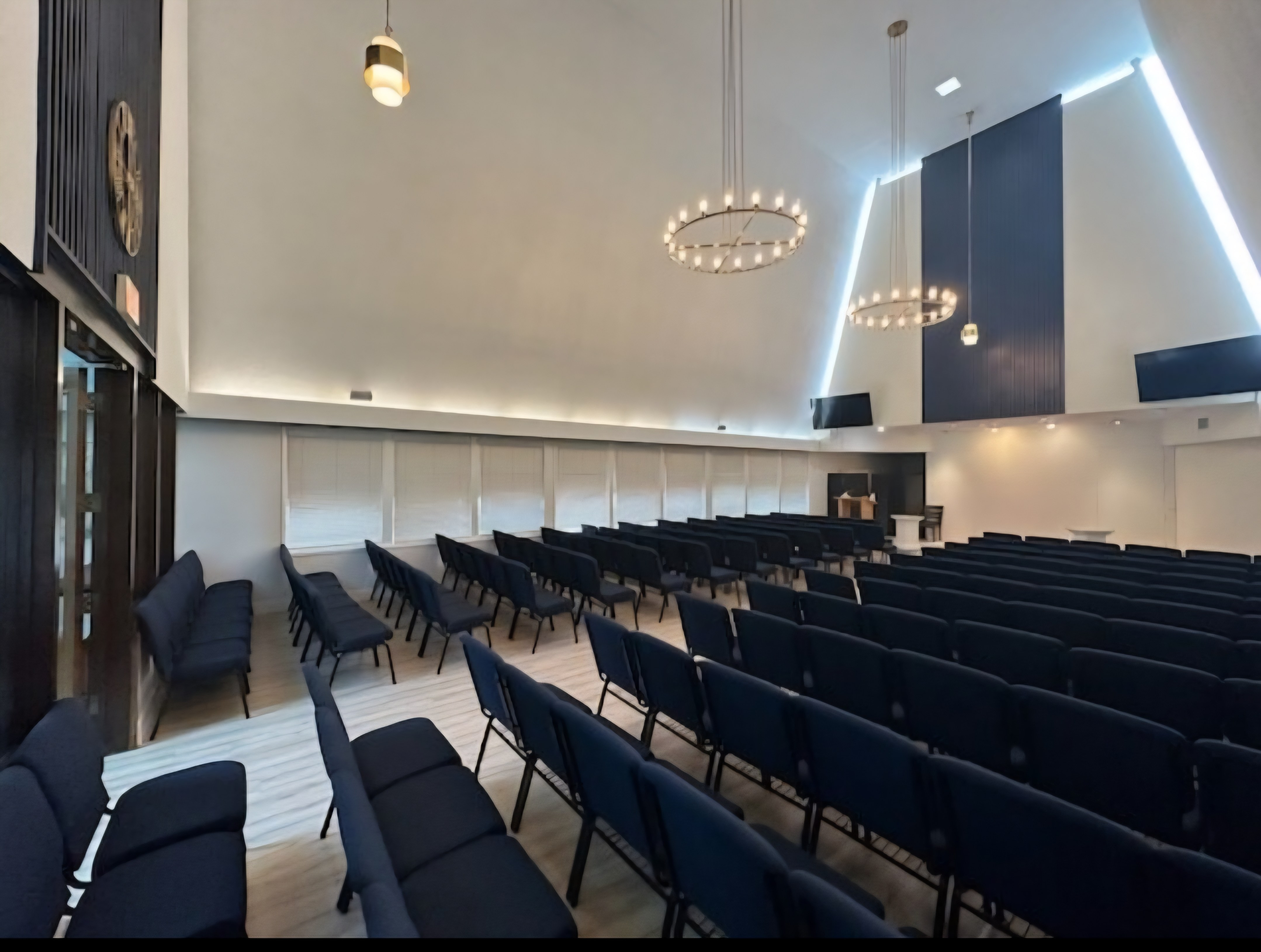Empty chapel interior at Destiny Funeral Home & Crematory with rows of dark blue upholstered chairs facing the entrance beneath a peaked ceiling and tiered chandeliers.