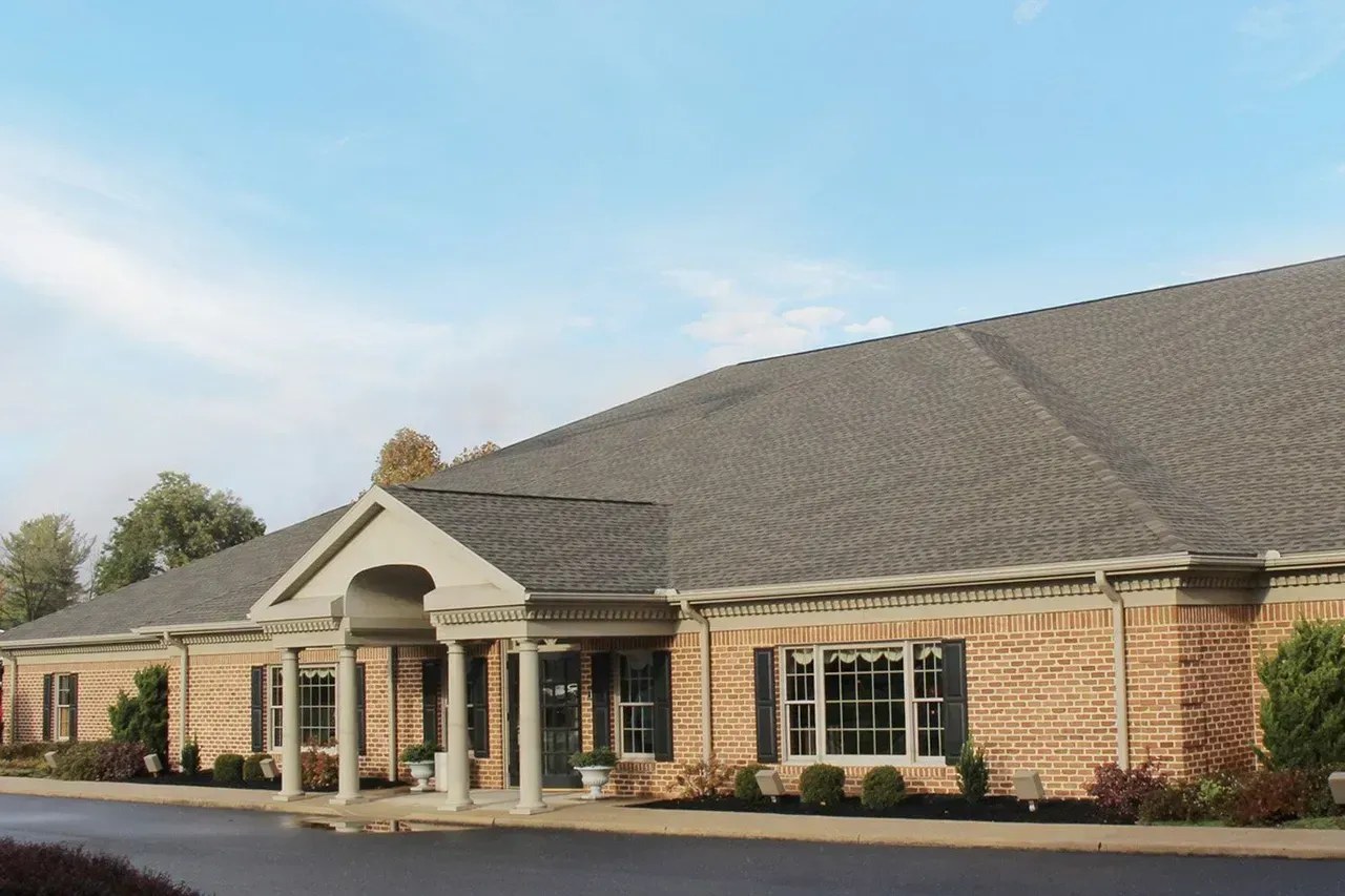 Thomas L Geisel Funeral Home's single-story brick building with a columned entrance portico under a partly cloudy autumn sky.