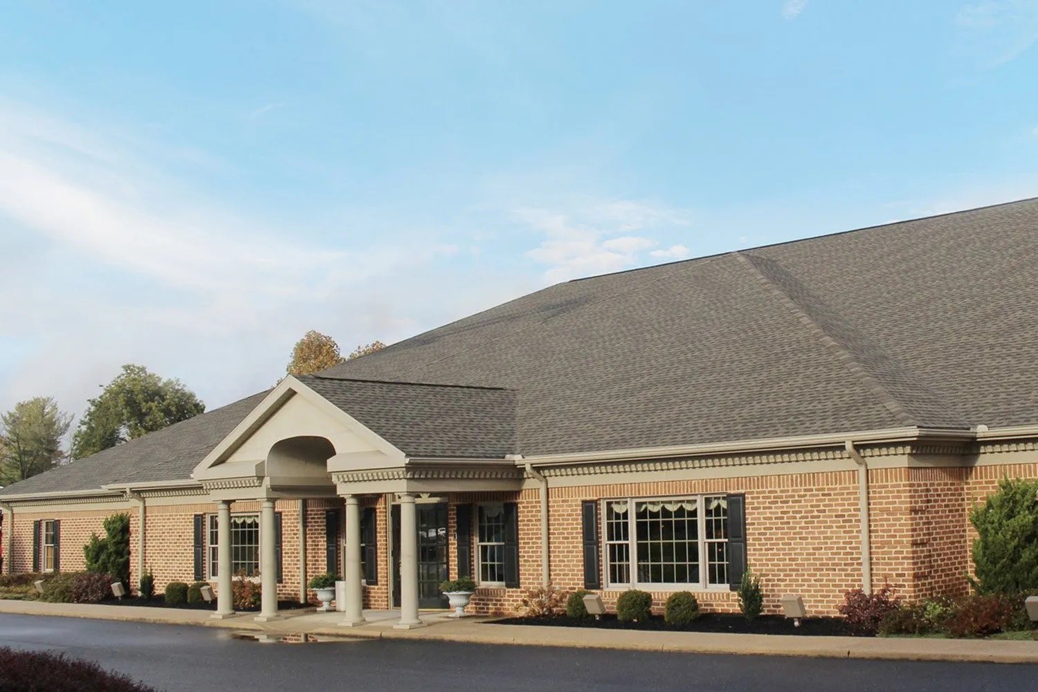 Thomas L Geisel Funeral Home's single story brick building with a columned entrance portico under a partly cloudy autumn sky