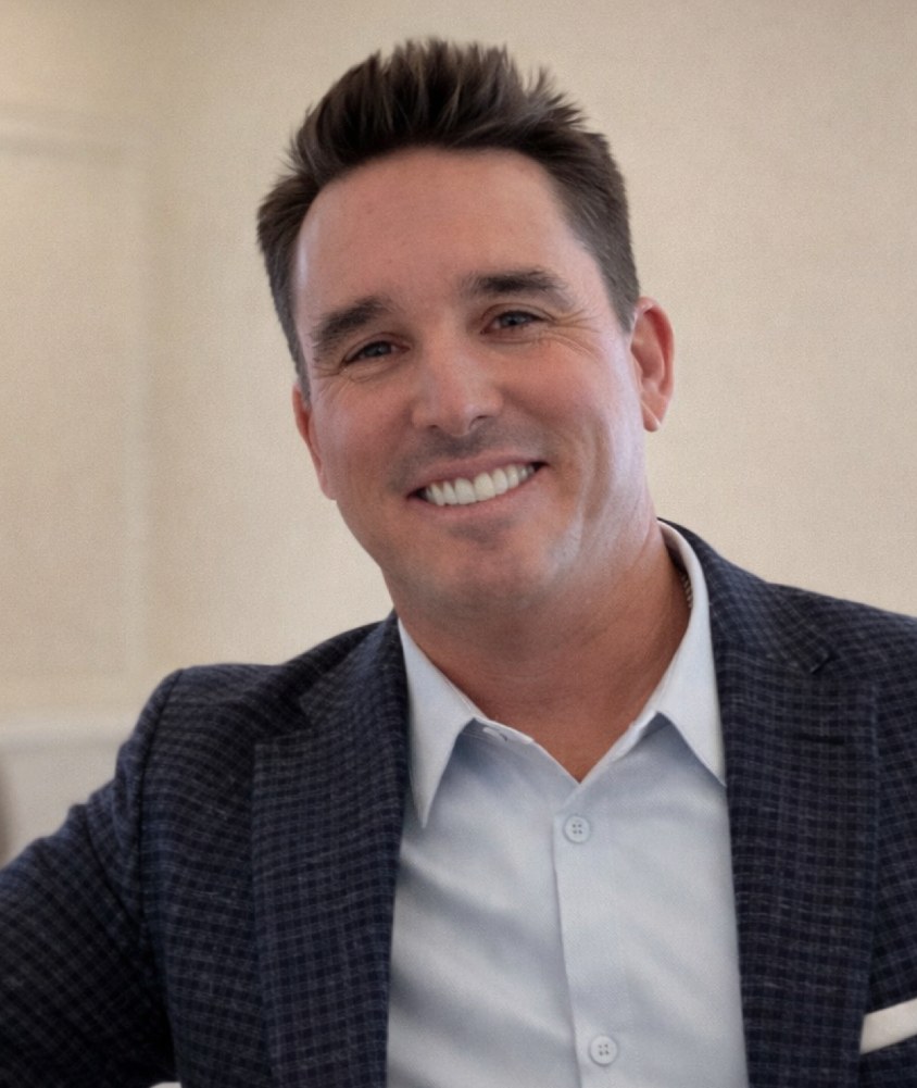 A smiling man in a checked blazer poses for a professional portrait.