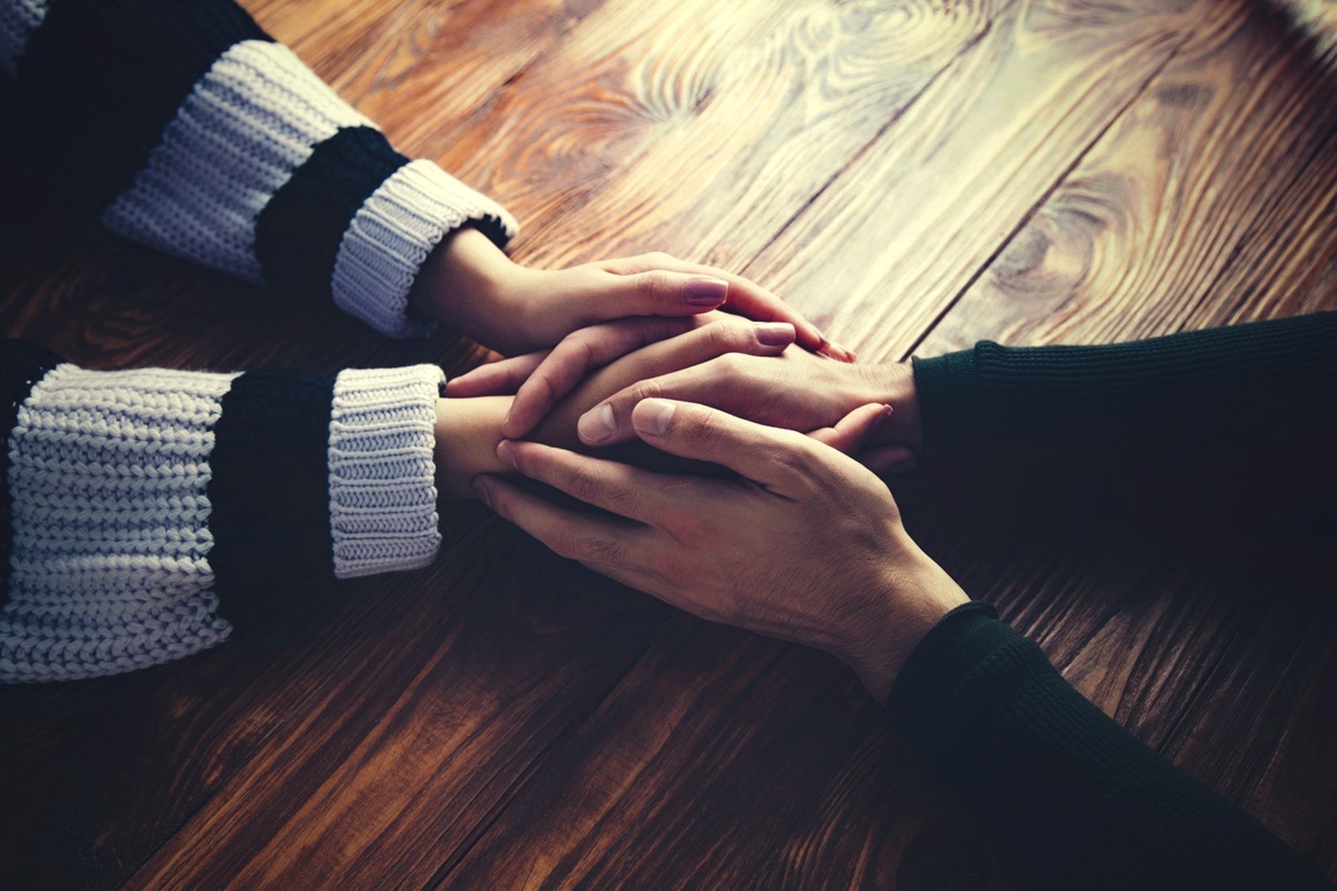 Close-up of an elderly person's clasped hands resting on a blue satin garment, indoors.