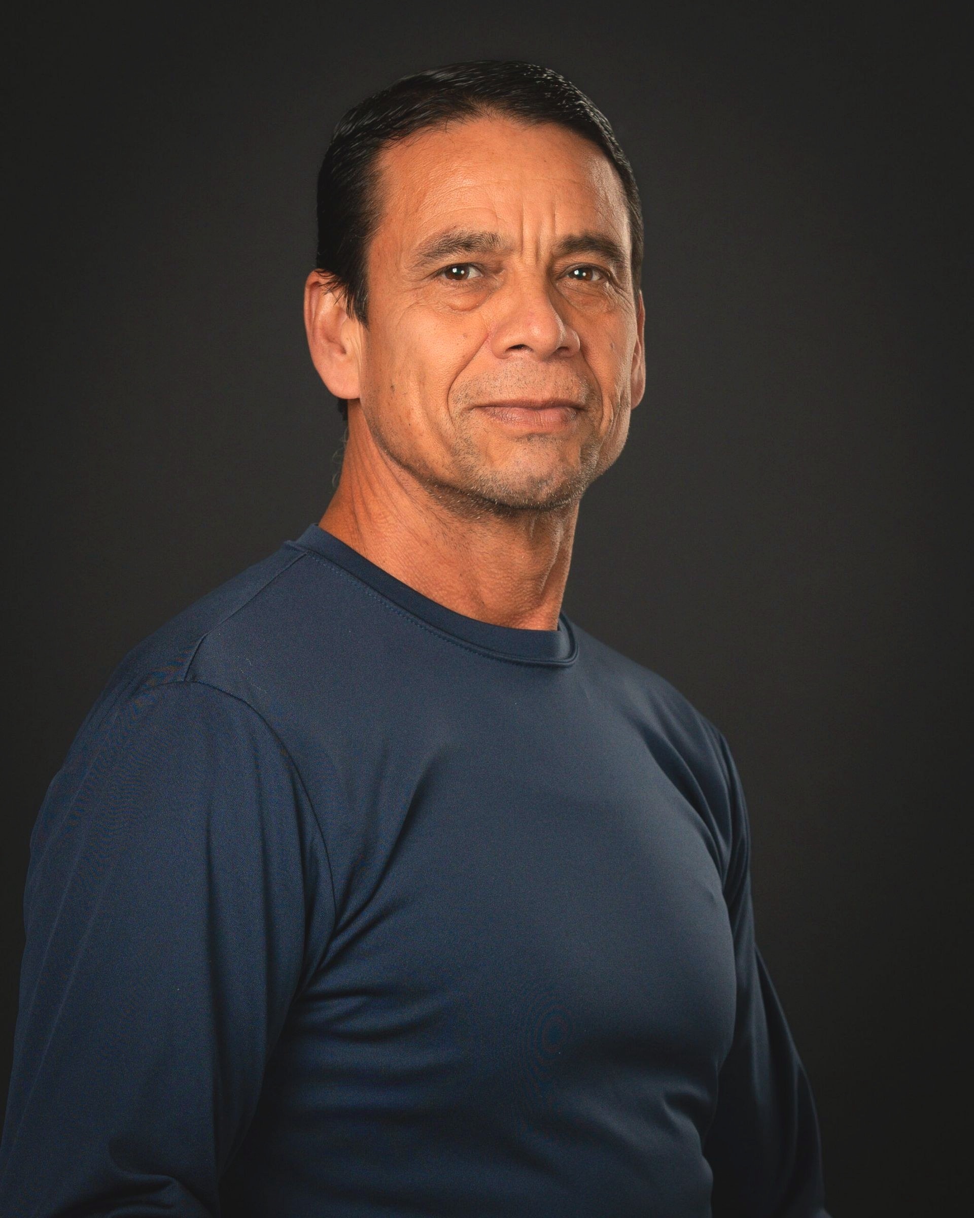 A funeral home staff member in a calm, composed studio portrait wearing a navy long-sleeve shirt.