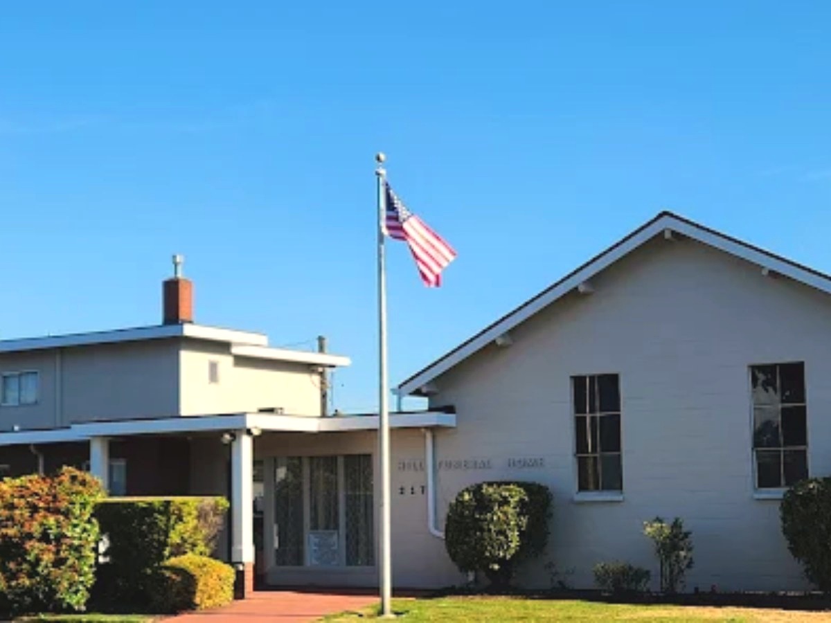 Valley Burial & Cremation's single-story funeral home building with an American flag and trimmed shrubs under a clear blue sky.