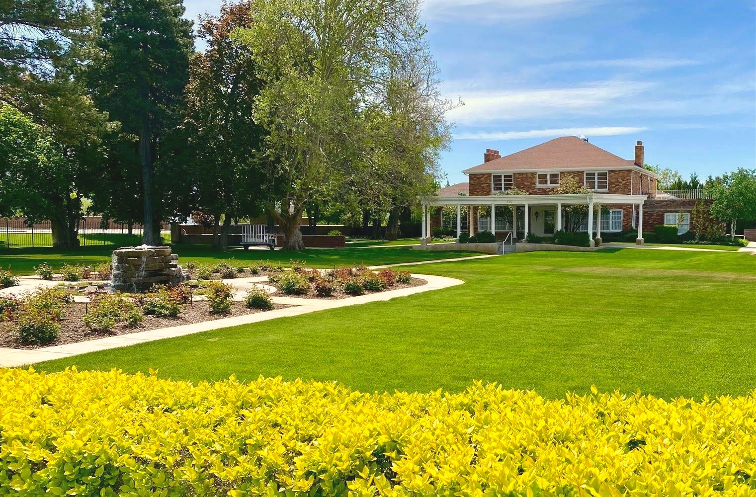 The Walker Sanderson Funeral Home building, a brick colonial-style structure with white columns, a covered porch, and landscaped grounds with a stone water feature.