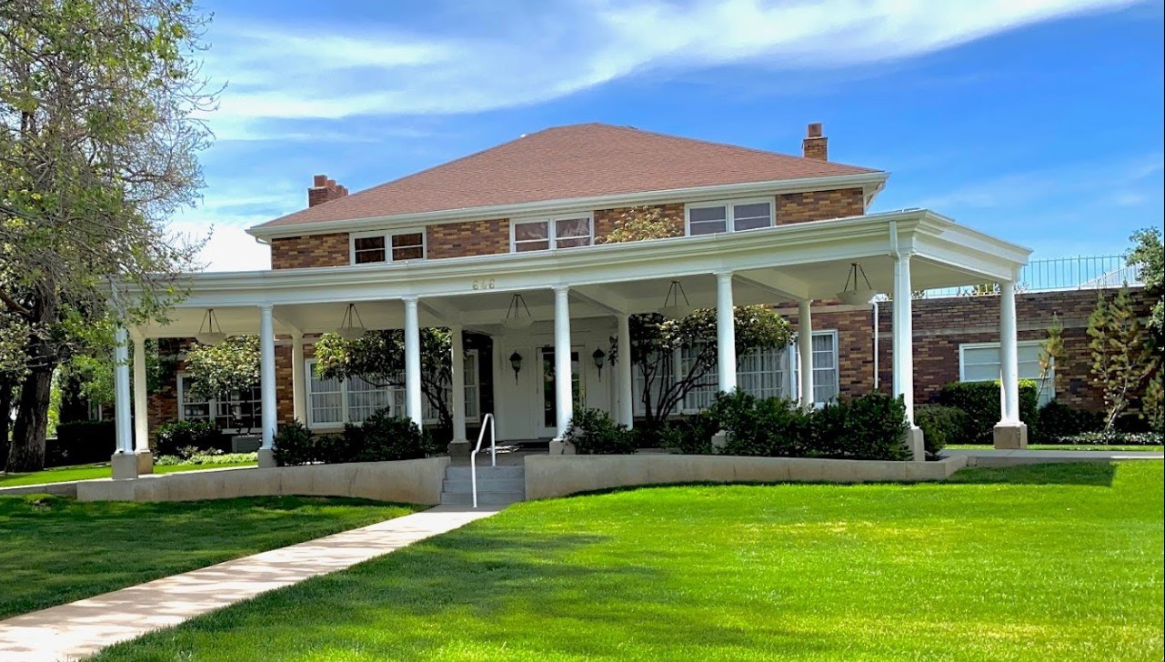 Brick colonial-style exterior of Walker Sanderson Funeral Home with a landscaped lawn, garden beds, and a stone water feature on a sunny day.