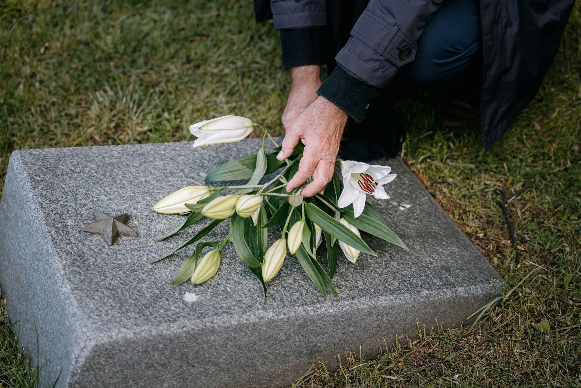 A lit red memorial candle and a bunch of red carnations resting on a gravestone