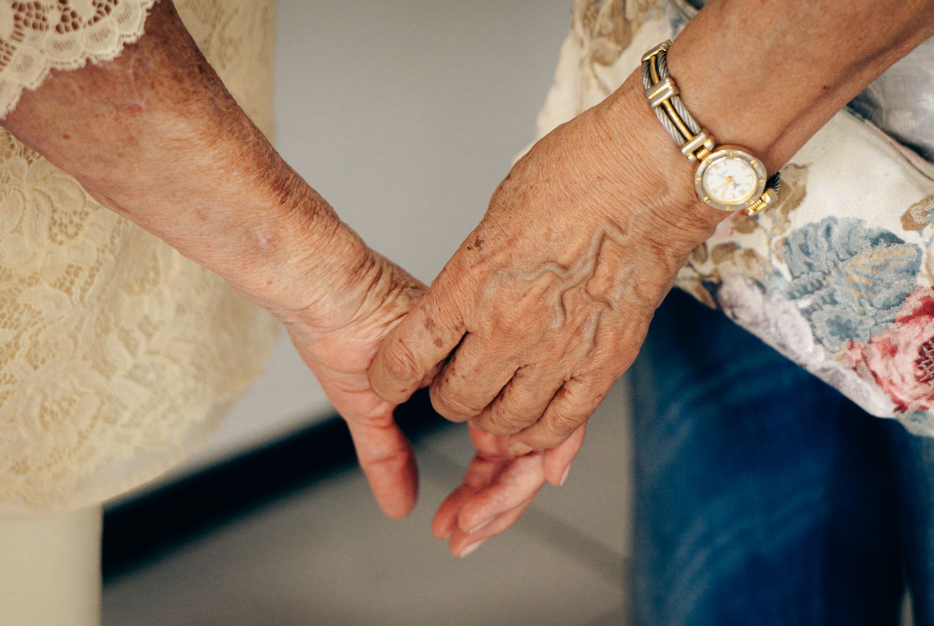 A close up black and white photo of two elderly hands clasped together, one wearing a ring, symbolizing lifelong companionship and care.