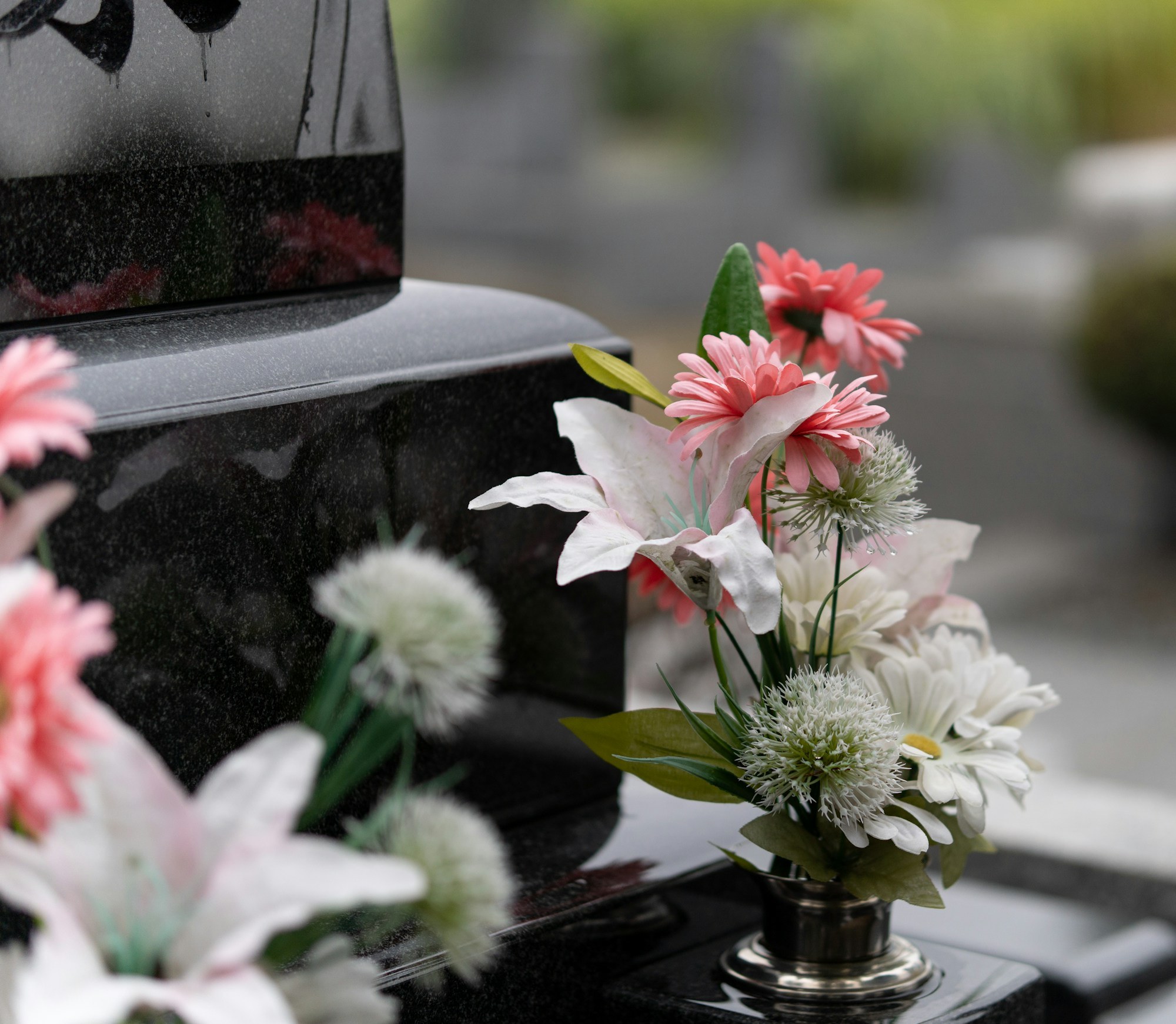 Flat memorial markers with small floral tributes are arranged in rows on a sloped, shaded cemetery lawn.