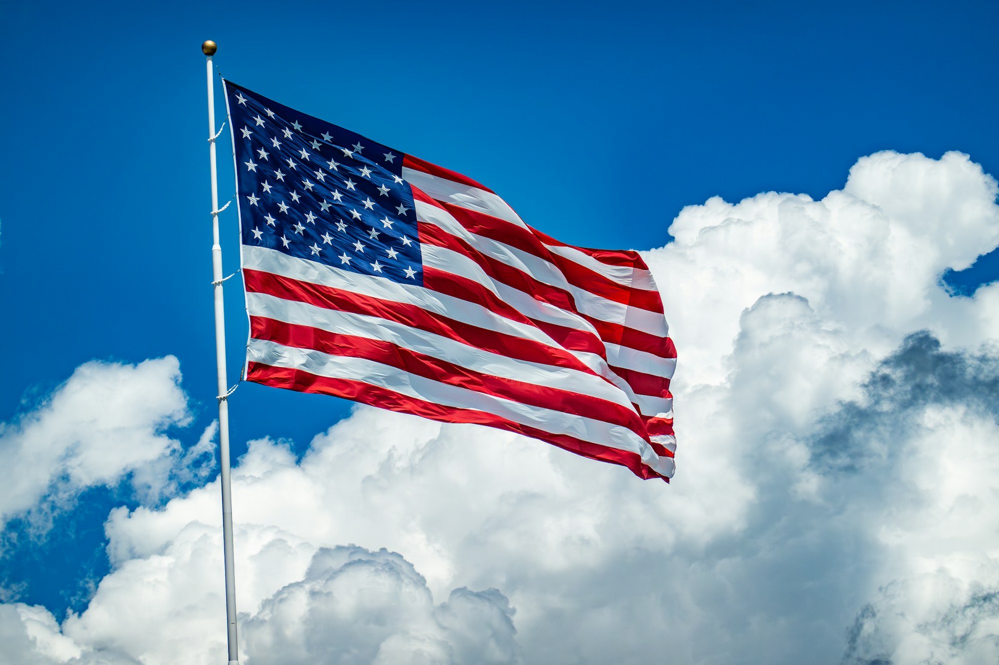 An American flag flying on a white pole against a bright blue sky with large white clouds
