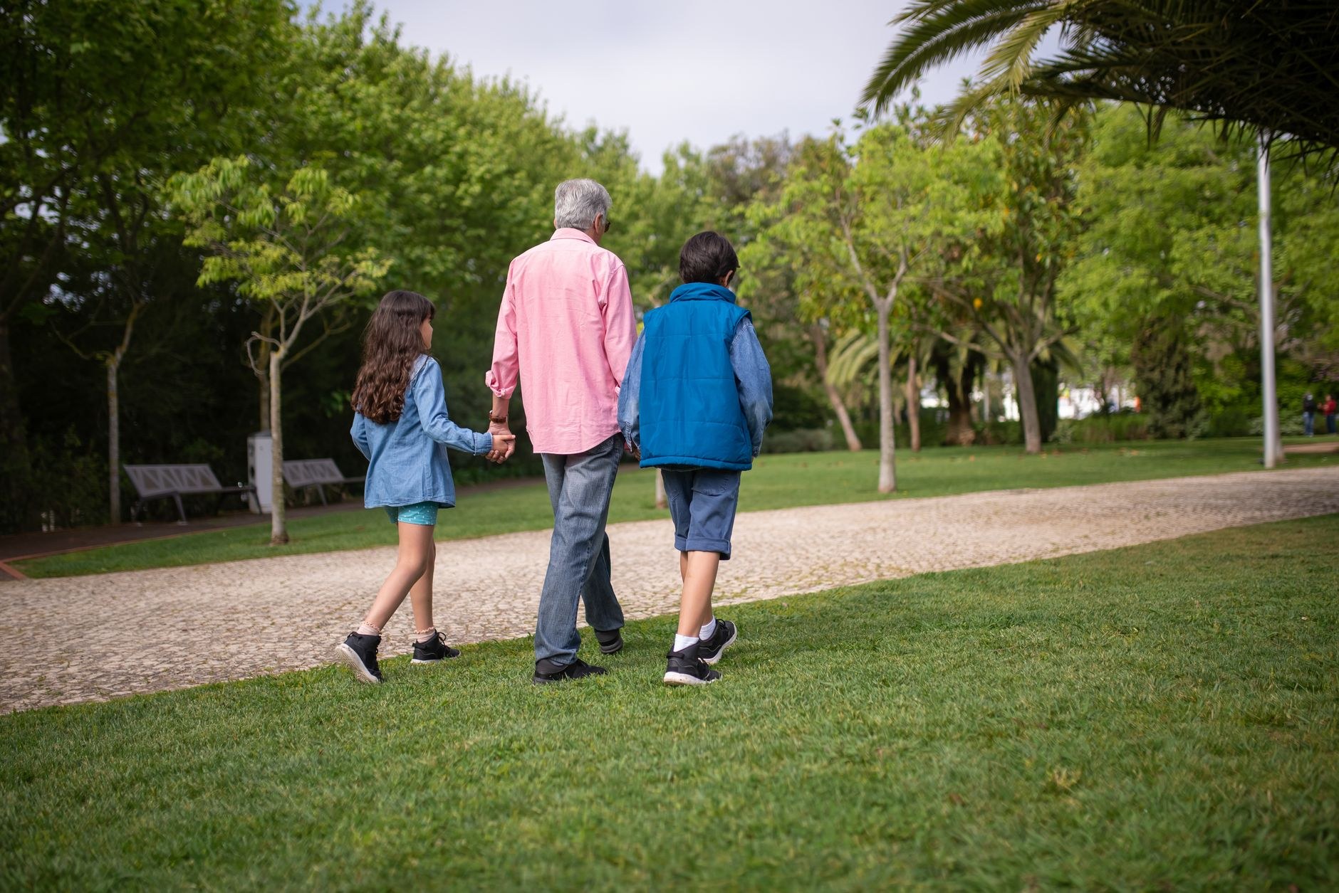 A family of four, including two children and two older adults, walks away from the camera along a paved path through bare winter trees near a lake.