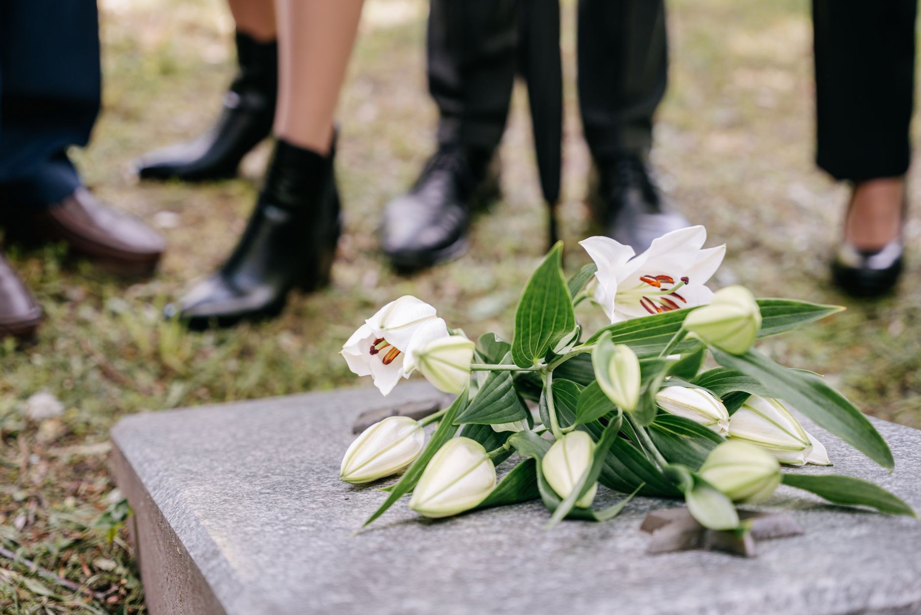 Rows of white military headstones on a cemetery lawn with two small flower arrangements placed at one grave.