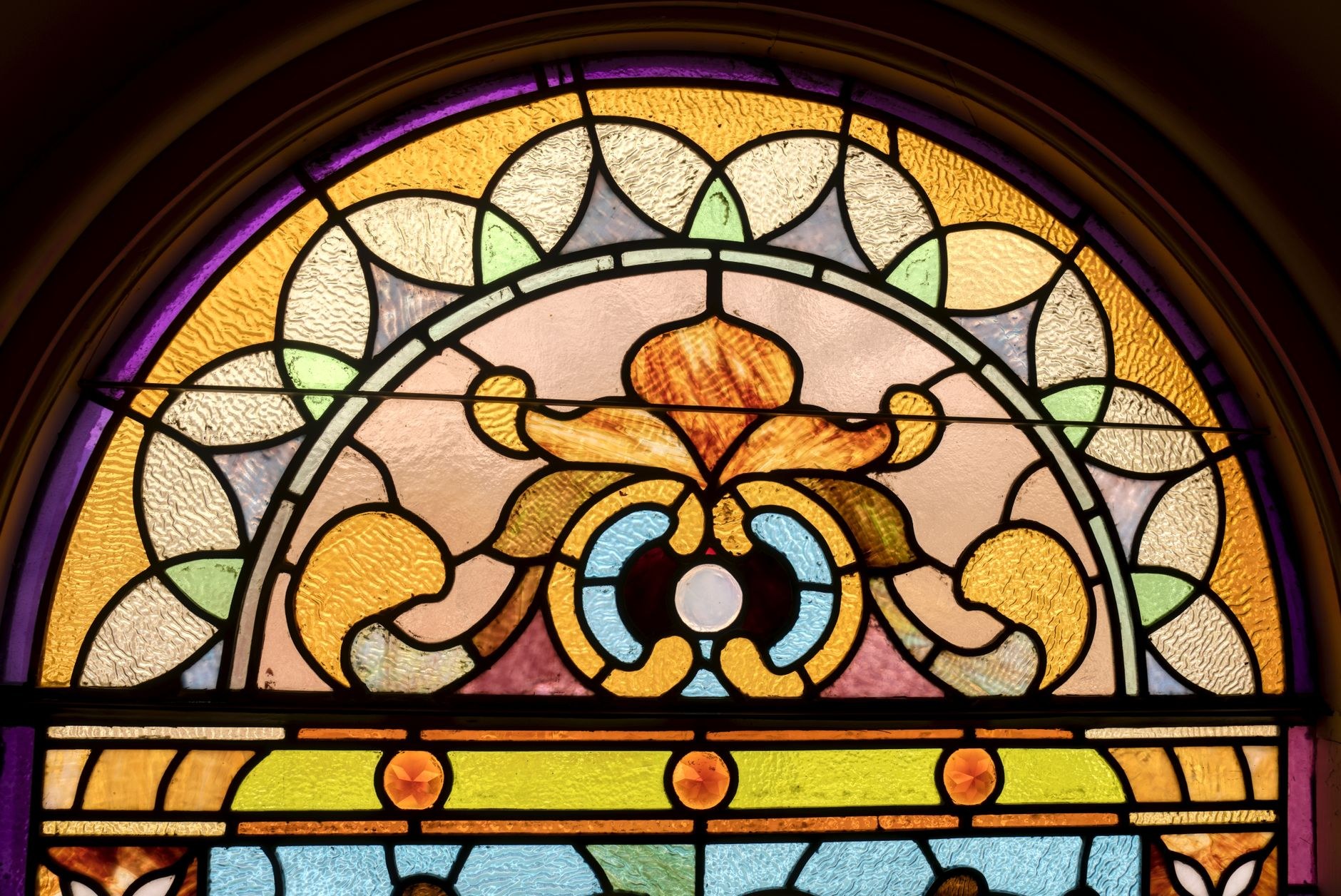 An arched window niche in a whitewashed wall frames a view of distant hills, with a sheer curtain half drawn across the glass.