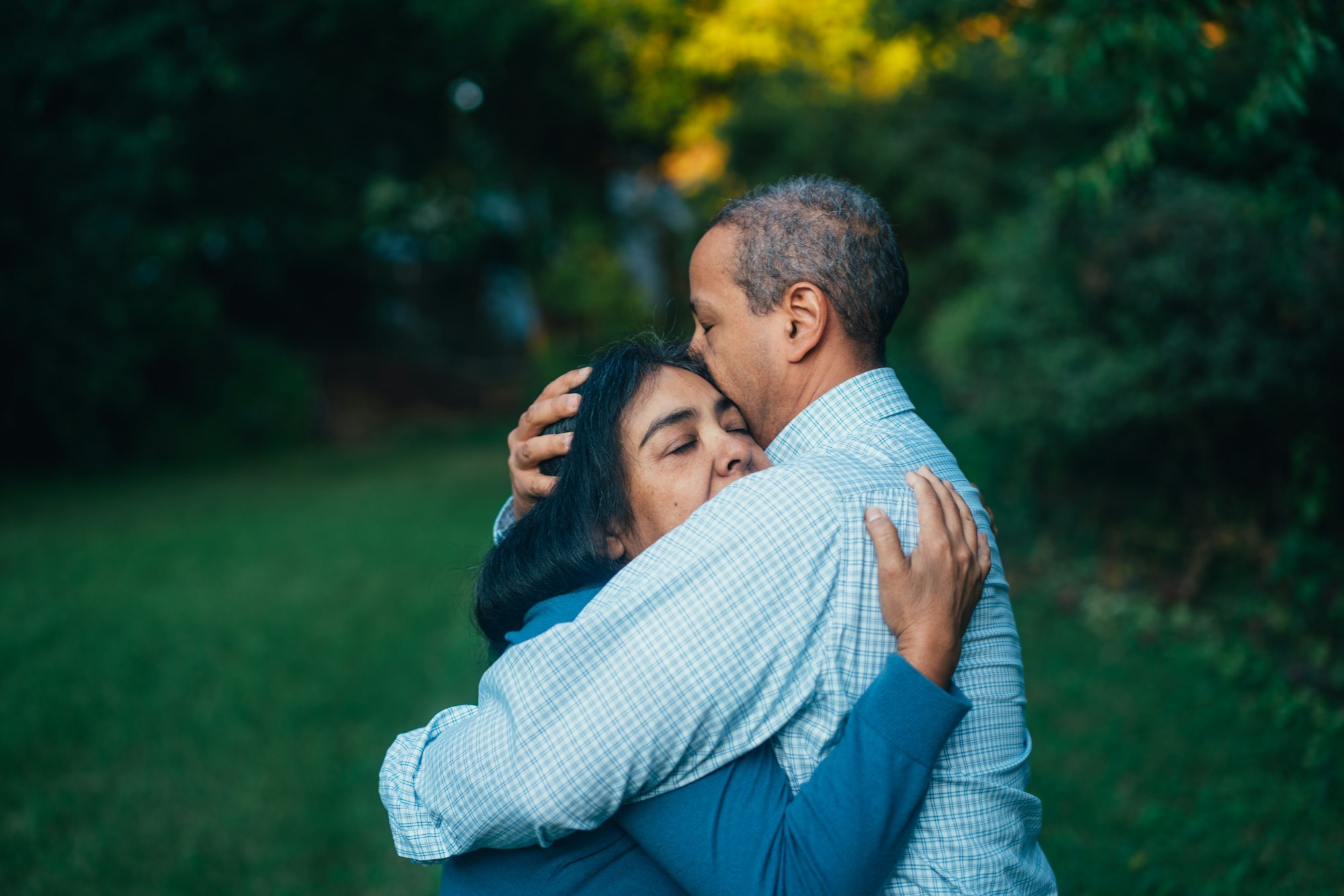 An older man and woman embracing tightly outdoors, comforting each other during a difficult time.